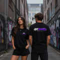 Two people wearing black t-shirts with a brand logo in an urban setting with graffiti.